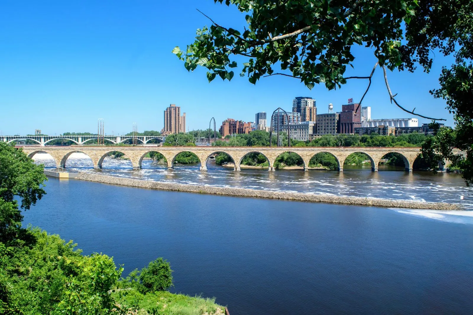 The Minneapolis skyline behind a stone arch bridge over the river