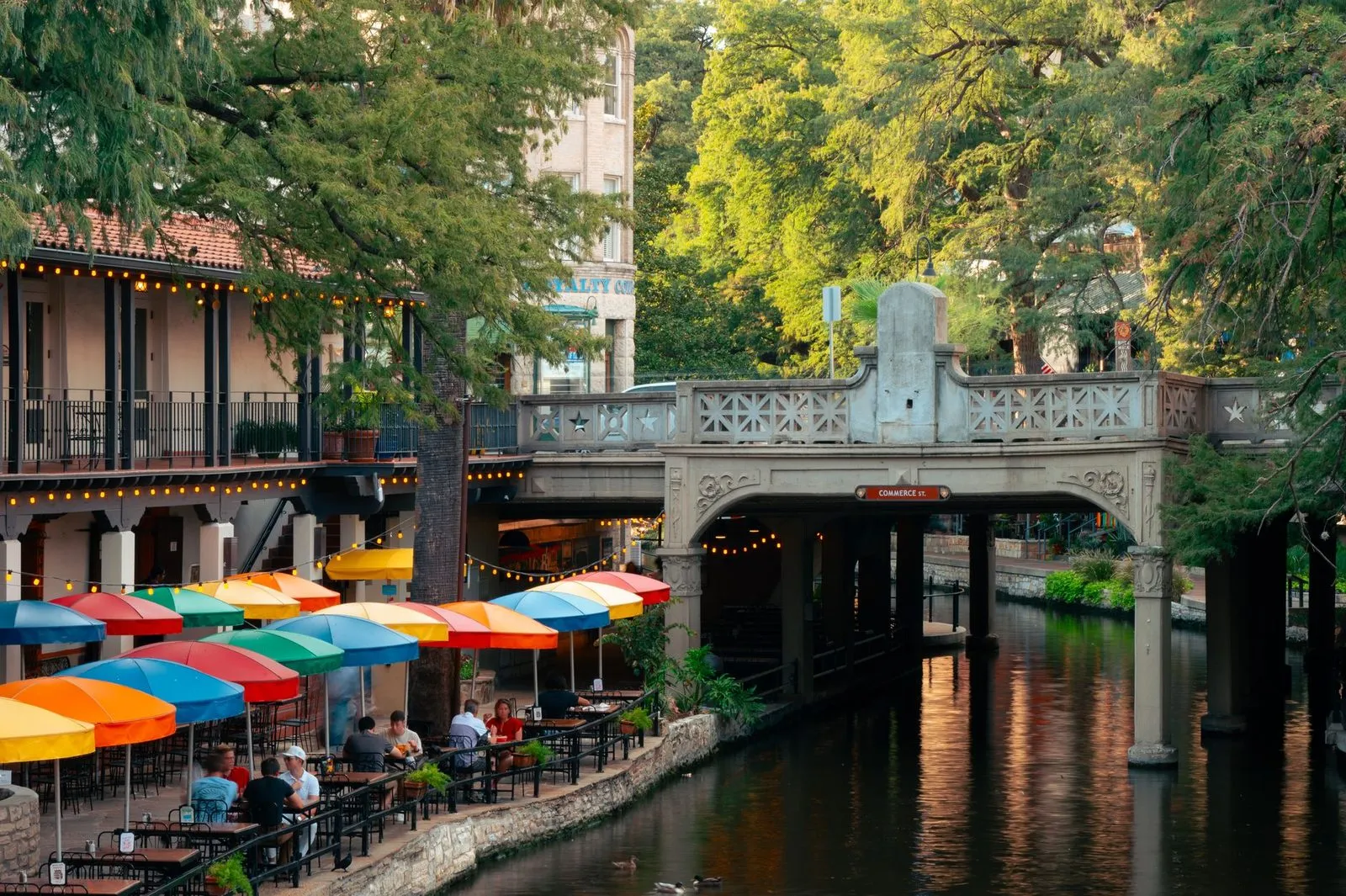 Umbrella tables along a canal walkway below street level on the San Antonio River Walk