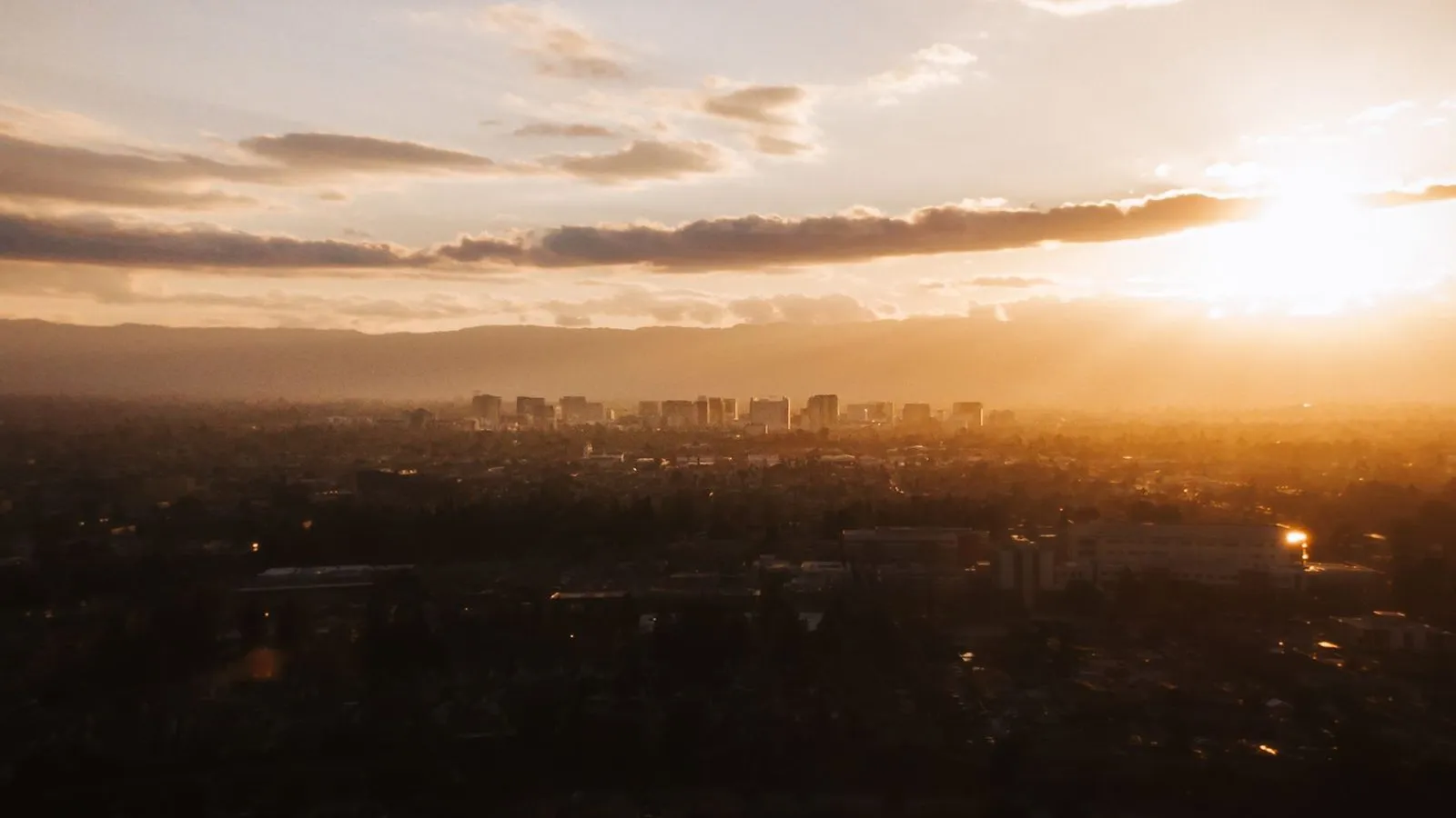 An aerial view of the San Jose skyline under a low golden sun